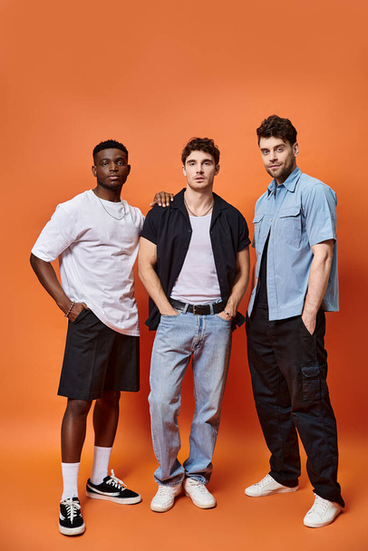 good looking diverse men in stylish urban clothes posing on orange backdrop, fashion concept - Photo, Image