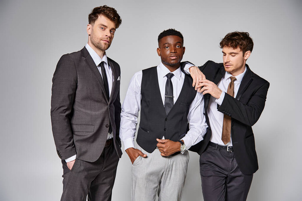 atractivos jóvenes amigos multiculturales en trajes de negocios inteligentes posando juntos sobre un fondo gris - Foto, imagen