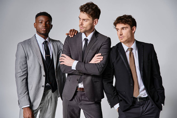 atrakcyjne młody międzyrasowy przyjaciele w inteligentny biznes garnitury pozowanie razem na szarym tle - Zdjęcie, obraz