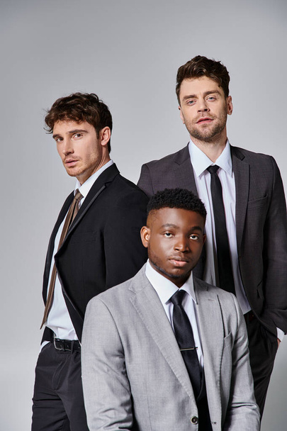 appealing young diverse friends in smart business suits posing together on gray background - Photo, Image