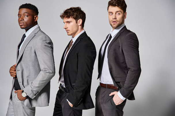 attractive stylish multicultural male models in business casual attires posing on gray backdrop - Photo, Image