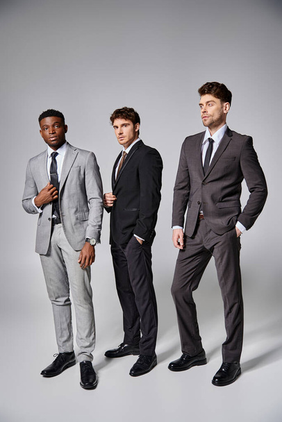 aantrekkelijke stijlvolle multiculturele mannelijke modellen in het bedrijfsleven elegante smart suits poseren op grijze achtergrond - Foto, afbeelding