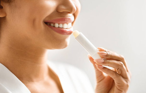 Lip Care. Unrecognizable young black woman applying moisturising chapstick on lips, closeup of smiling african american female using nourishing lip balm while making beauty routine at home, cropped - Photo, Image