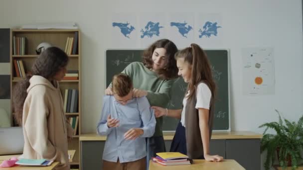 Grupo de tres matones adolescentes que rodean al chico nerd pellizcándolo, pinchándolo e insultándolo durante el descanso en la escuela - Metraje, vídeo