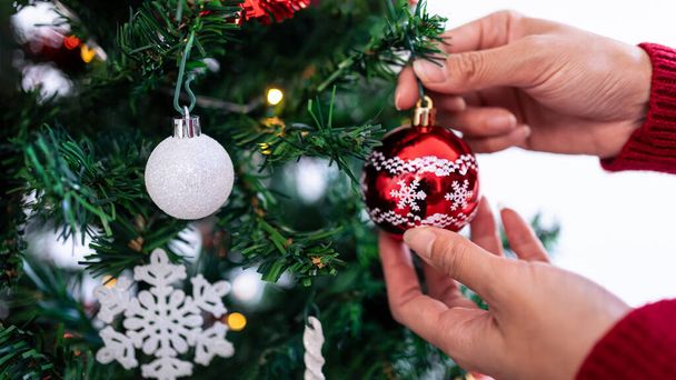 Boldog karácsonyt és boldog ünnepeket, egy nő keze díszíti a fenyőfát otthon télen. Karácsonyi piros golyó lóg fenyő ágak dekoráció banner, Szilveszter koncepció. - Fotó, kép