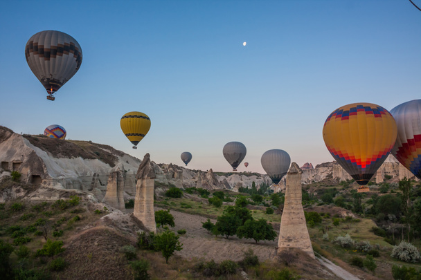 Hot air balloons flying over bizarre rock landscape in Cappadocia. Balloons fly early in the morning. Beautiful hot air balloons in the morning sky. Moon in the sky. Goreme. Turkey - Photo, Image