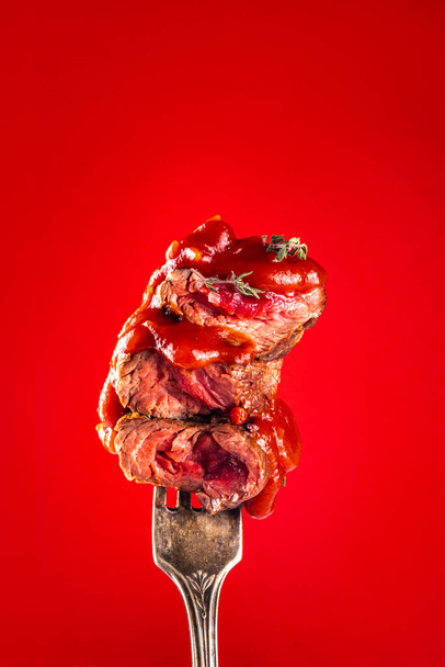 Izgara biftek parçaları, orta pişmiş, çatallı, baharatlı, tuzlu, otlu ve ketçaplı. Parlak kırmızı arkaplanda, alanı kopyala - Fotoğraf, Görsel