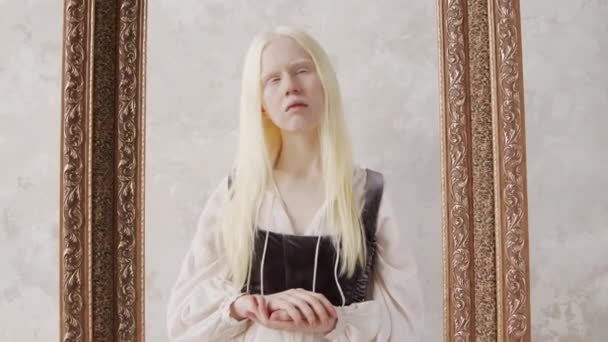 Zoom in studio portret van jonge albino vrouw in vintage witte jurk met korset-stijl top poseren op camera in fotolijstje - Video