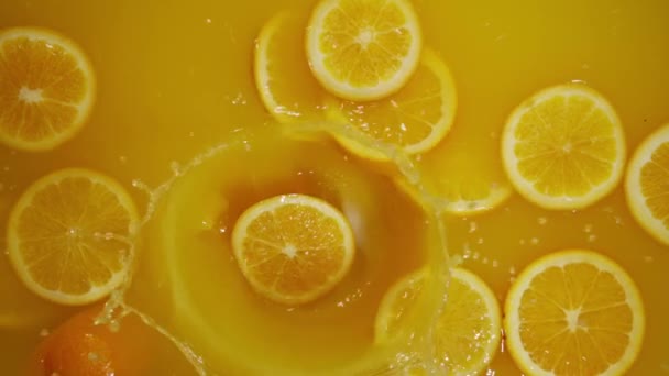 Close-up van vallende gesneden limoenen, sinaasappelen en citroenen in het water op oranje achtergrond, maken van een cocktail van citrusvruchten, drinken van koude limonade, schieten van koolzuurhoudend water met gesneden vruchten. - Video