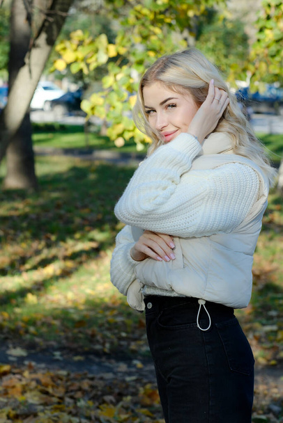 Portret młodej pięknej blondynki z długimi włosami w białym swetrze i kurtce słonecznej jesieni w parku miejskim - Zdjęcie, obraz