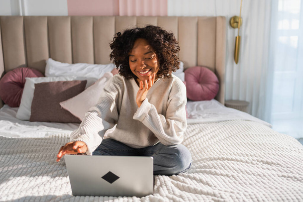 アフリカ系アメリカ人の少女は,自宅のオフィスのベッドでラップトップを使用して,電子メールを読むチャットをタイプします. オンラインチャットビデオ通話会議の仮想会議を持つ若い黒人女性. 自宅から学ぶ仕事 - 写真・画像