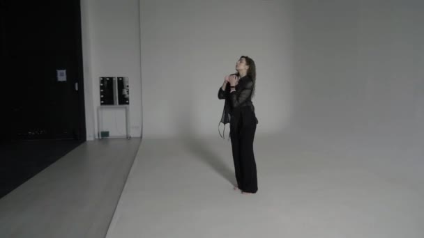 Hermosa mujer rizada sexy de moda en ropa negra baila lentamente descalza en un cyclorama blanco en el estudio de fotos - Metraje, vídeo