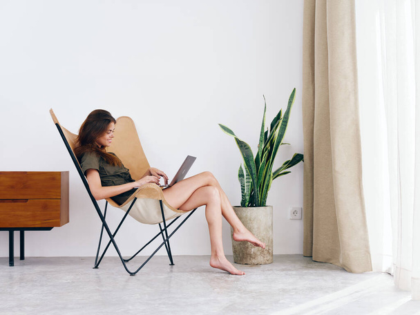 Женщина, сидящая в кресле с ноутбуком и смотрящая кино и социальные сети у себя дома, улыбается, современный стильный интерьер скандинавского образа жизни, копирует пространство. Высокое качество фото - Фото, изображение