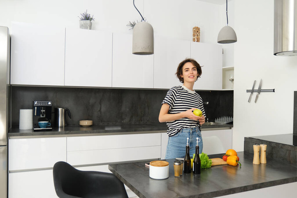 Portret van een gelukkige, gezonde jonge vrouw, vegetariër die salade voor zichzelf maakt, poseert in de buurt van groenten in de keuken, hakt ingrediënten voor veganistische maaltijd. - Foto, afbeelding