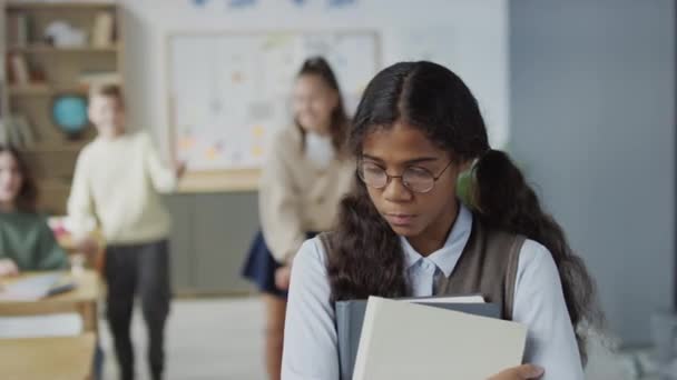 Selective focus shot of teen African American girl wearing eyeglasses holding books suffering bullying at school - Footage, Video