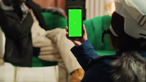Persoon maakt gebruik van smartphone met greenscreen en genieten van gesprek met vriendje, het tonen van lege chromakey display op de telefoon. Afwisselend koppel in het alpine skigebied tijdens de winter. - Video