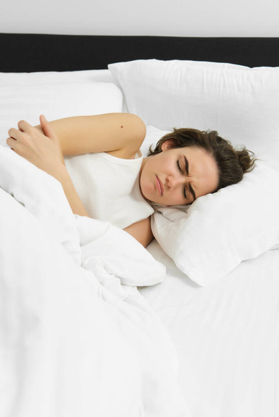 Portrait of woman lying in bed with stomach ache, has menstrual cramps, frowning and feeling pain period. Wellbeing and health concept - Photo, Image