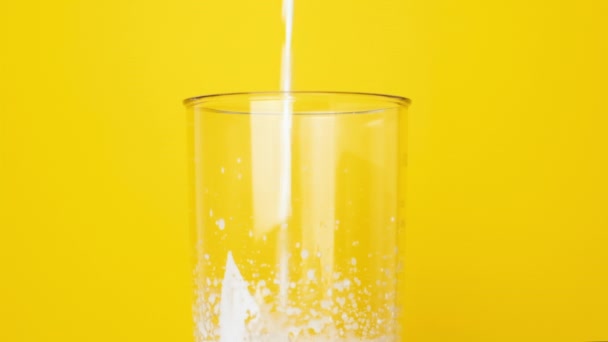 O leite é derramado em um copo para fazer um batido caseiro. O leite é derramado em um copo de um liquidificador em um fundo amarelo brilhante.. - Filmagem, Vídeo