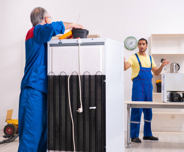 De twee aannemers repareren koelkast in werkplaats - Foto, afbeelding