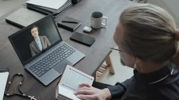 Vista de ángulo alto del sacerdote católico consultando a un joven que estudia teología durante una videollamada en computadora portátil - Metraje, vídeo