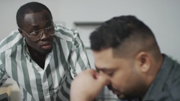 Επιλεκτική φωτογραφία εστίασης του αλαζονικού Αφροαμερικανού που προσβάλλει καταθλιπτικό συνάδελφο από τη Μέση Ανατολή στην εργασία - Πλάνα, βίντεο