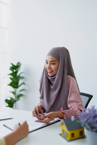 Una empleada del banco musulmana, haciendo un acuerdo sobre un préstamo residencial con un cliente - Foto, imagen