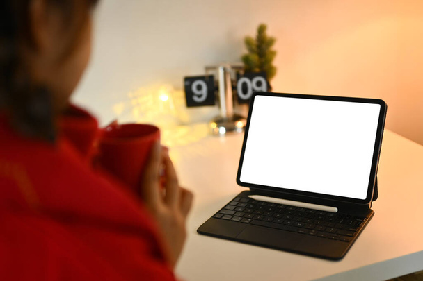 Mladá žena pije horký čaj a pomocí digitální tablet v stydlivém obývacím pokoji. - Fotografie, Obrázek