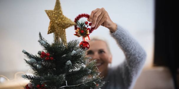 Mujer anciana alegre caucásica decorar el árbol de Navidad. Ambiente de Navidad en el acogedor interior del hogar. - Foto, Imagen
