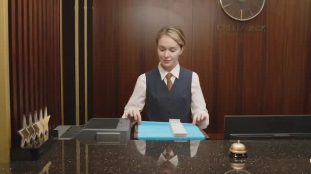 Medium shot portret van jonge vrolijke receptioniste staande op de werkplek in uniform en kijkend naar de camera - Video