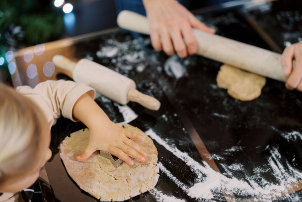 La petite fille presse un coupe-biscuits sur une pâte à côté de sa mère déroulant la pâte. Photo de haute qualité - Photo, image