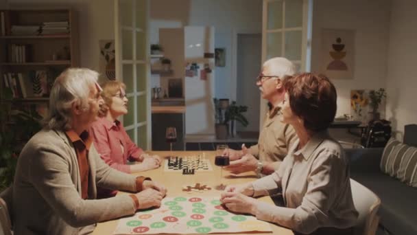 Средний снимок положительных пенсионеров, сидящих за большим столом и выясняющих, кто они в угадывании игры на домашней вечеринке - Кадры, видео
