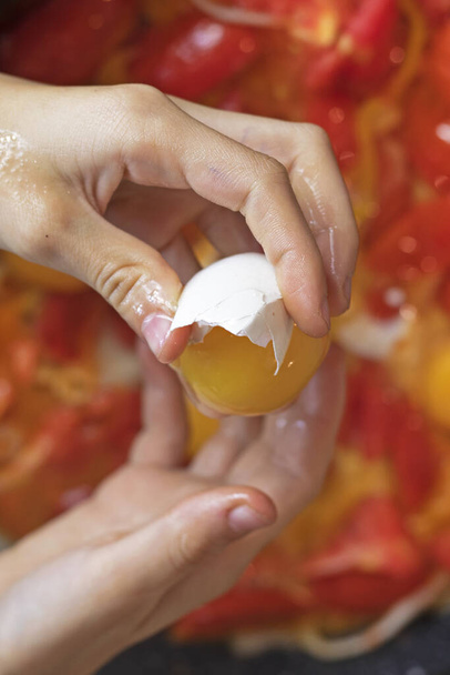  drží v ruce kuřecí vejce, aby ho rozbila. vaření míchaných vajec s rajčaty - Fotografie, Obrázek