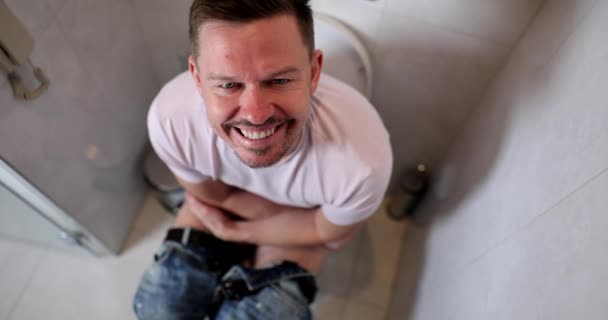 Hymyilevä mies istuu vessassa hidastettuna. Ulostamisongelmat, miesten terveys, matala painopiste - Materiaali, video