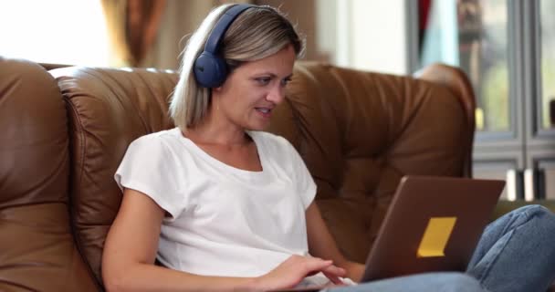 ソファの上のヘッドフォンの女性はノートパソコン、クローズアップを使用しています。遠くの仕事、ガジェットで余暇を楽しむ - 映像、動画