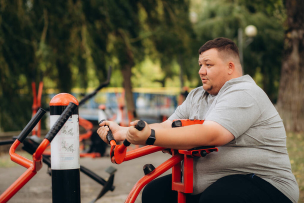 um homem gordo balança em máquinas de exercícios no parque - Foto, Imagem