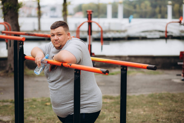 un uomo grasso beve acqua e perde chili facendo sport - Foto, immagini
