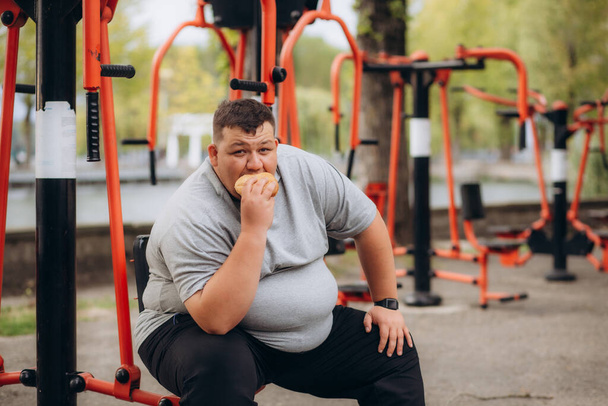 een dikke man eet een hamburger na het sporten - Foto, afbeelding