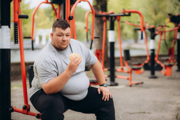 太った男が公園の遊び場でハンバーガーを食べる - 写真・画像