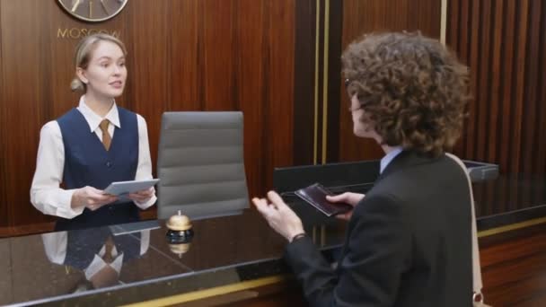 A vállára néző nő kérdezi rendszergazda a rendelkezésre álló szobák a szállodában, és így útlevél bejelentkezni - Felvétel, videó