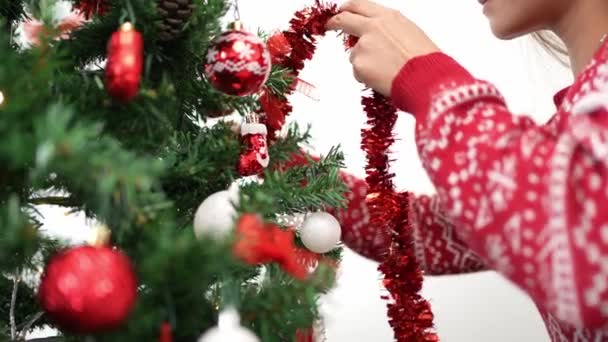 Frohe Weihnachten und frohe Feiertage, Hand einer asiatischen Frau schmückt die Fichte mit einem Lametta-Kranz, zu Hause im Winter. Weihnachtskugel aus Tannenzweigen zur Dekoration - Filmmaterial, Video