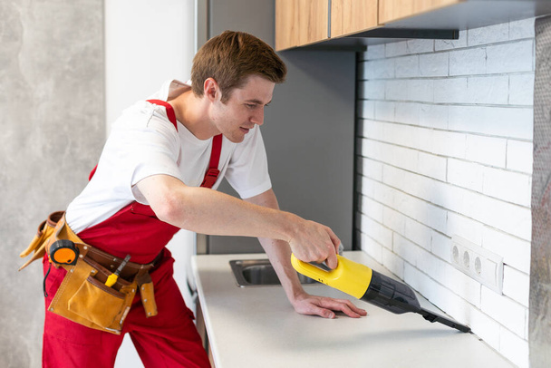 Genç yakışıklı adam evi temizliyor. Çekici adam mutfakta elektrikli süpürge tutuyor.. - Fotoğraf, Görsel