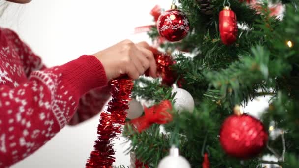 Rallentatore di donna asiatica decorazione albero di Natale con fili di lame ghirlanda in casa stanza. Buon Natale e felice anno nuovo concetto. Ragazza mettendo ornamenti di Natale su rami di abete rosso. Momenti familiari accoglienti - Filmati, video