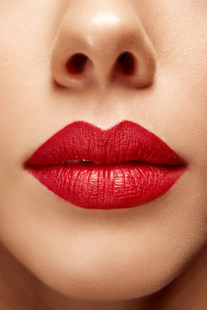 Extremo de cerca la foto de lleno regordeta labios femeninos de color rojo brillante. Boca vestida. Lápiz labial mate. Rutina de cuidado. Concepto de belleza, maquillaje, cosmetología, tratamientos de spa, productos cosméticos. Anuncio - Foto, imagen