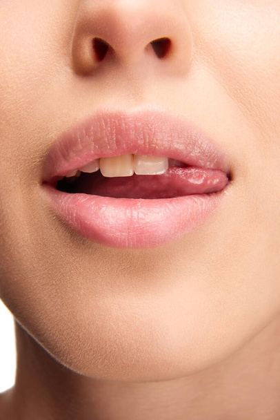 Open mond, tong raakt tanden. Close-up uitzicht van de vrouw likken roze natuurlijke glans lippen. Mooie mollige lippen. Concept van schoonheid, make-up, cosmetologie, spa-behandelingen, cosmetische producten, glamour. Steun - Foto, afbeelding