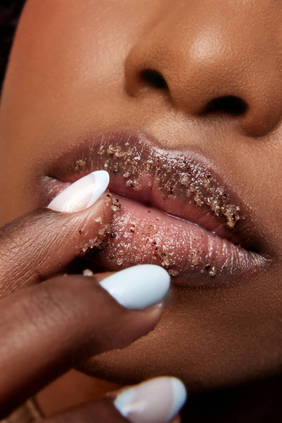 Vista de cerca de la mujer afroamericana con los labios llenos de azúcar. Exfoliar el tratamiento de spa para los labios. Concepto de belleza, maquillaje, cosmetología, tratamientos de spa, productos cosméticos. Anuncio - Foto, Imagen