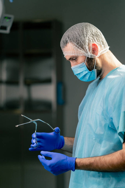 Close-up shot of a doctor surgeon in a special uniform preparing instruments before surgery in an operating room - Photo, Image