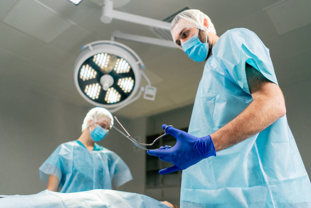 Ο χειρουργός παίρνει ένα αποστειρωμένο μεταλλικό νυστέρι για να ξεκινήσει την εγχείρηση στο χειρουργείο. - Φωτογραφία, εικόνα