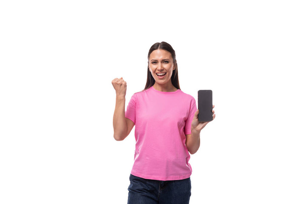 jeune belle femme intelligente aux cheveux noirs vêtue d'un t-shirt rose tenant un smartphone avec une publicité. - Photo, image