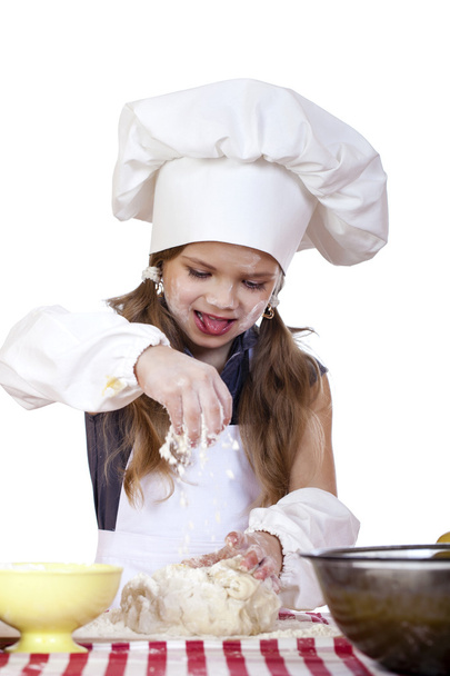 Little girl in a white apron and chefs hat knead the dough in th - Foto, Bild