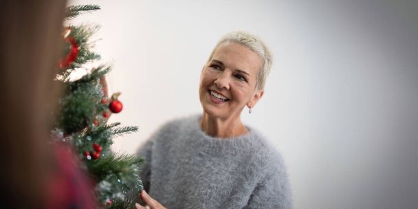陽気な高齢女性はクリスマスツリーをデコラートします. 居心地の良い家のインテリアでクリスマスの雰囲気. - 写真・画像